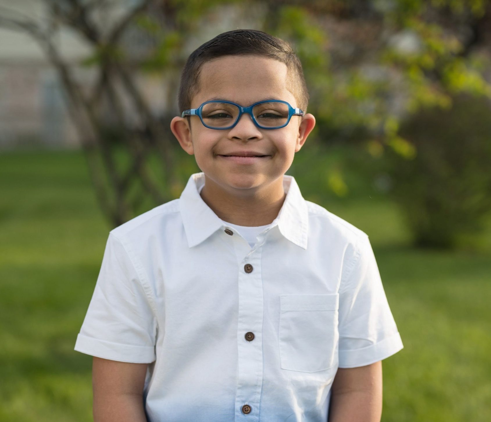 A smiling boy with Down syndrome in a white shirt, outdoors in spring