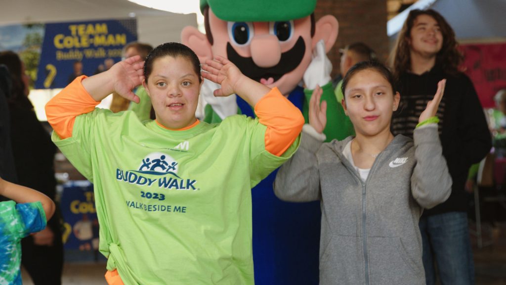 Teens in green DSANWI shirts cheering with a costumed character at an event