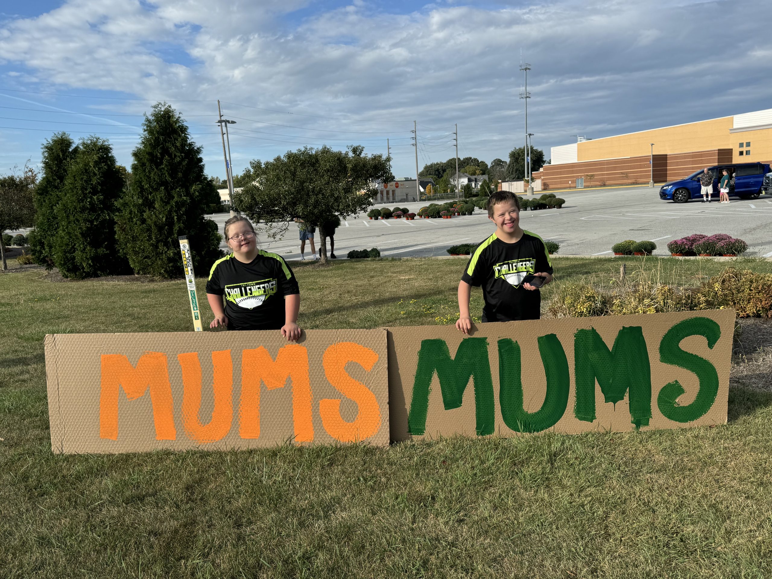 Two DSANWI kids holding hand-painted MUMS signs at the fall mum sale